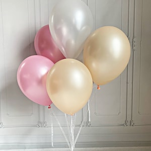 Puede incluir: Un grupo de cuatro globos en rosa, blanco y dorado atados con una cinta blanca. Los globos est&aacute;n dispuestos en forma de pir&aacute;mide con el globo blanco en la parte superior.