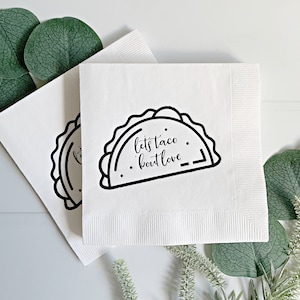 May include: White paper napkins with a black outline of a taco and the text "let's taco 'bout love".