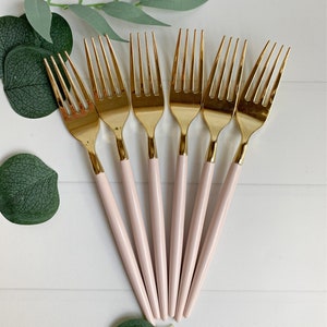May include: Set of six gold forks with pink handles. The forks are arranged in a fan shape with the handles pointing towards the bottom of the image.