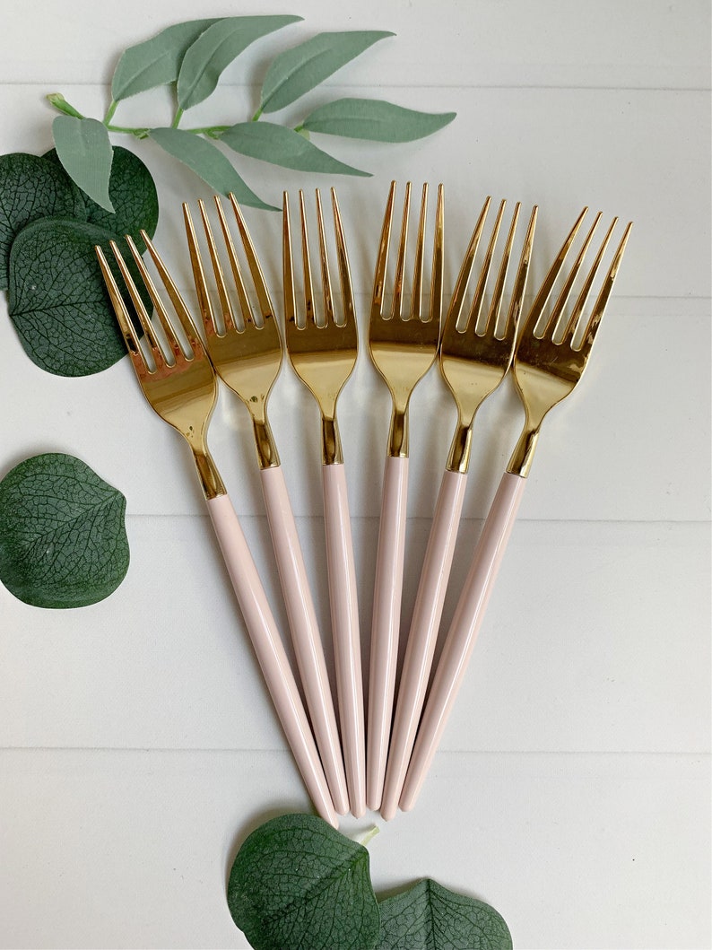 May include: Set of six gold forks with pink handles. The forks are arranged in a fan shape with the handles pointing towards the bottom of the image.