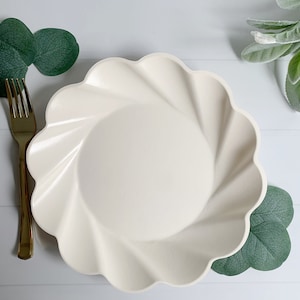 May include: A cream-coloured, scalloped-edge plate with a gold fork and green leaf accents. The plate has a spiral design in the centre. The arrangement suggests a setting for a meal or event.