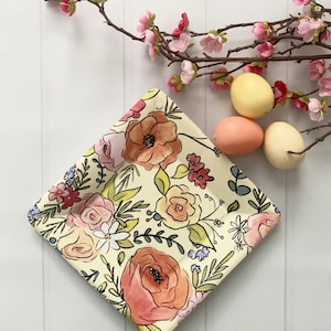 May include: A square, floral-patterned plate with a cream background and watercolor-style flowers in shades of pink, peach, and red. The plate is surrounded by pink blossoms and three decorative eggs.