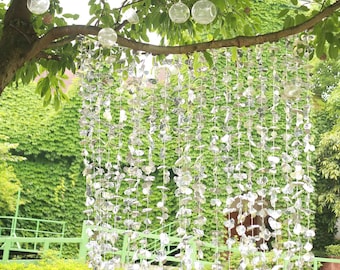 May include: A silver garland with shiny, reflective leaves hangs from a tree branch. The garland is made of many small, individual leaves that are connected together. The leaves are arranged in a cascading pattern, creating a beautiful and festive look.