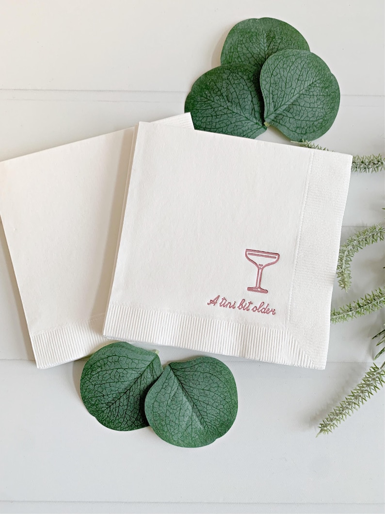 Celebrate a milestone in style with these charming A Tini Bit Older Martini Cocktail Napkins, the perfect addition to any martini-themed birthday party or sophisticated gathering. Designed for lovers of elegant cocktails, these foil-stamped napkins feature a chic illustration of a classic coup martini glass wrapped with a delicate bow around the stem, adding a playful yet refined touch to your celebration. These are perfect for any age birthday, give them as gift for the martini lover.