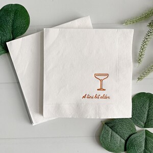 Celebrate a milestone in style with these charming A Tini Bit Older Martini Cocktail Napkins, the perfect addition to any martini-themed birthday party or sophisticated gathering. Designed for lovers of elegant cocktails, these foil-stamped napkins feature a chic illustration of a classic coup martini glass wrapped with a delicate bow around the stem, adding a playful yet refined touch to your celebration. These are perfect for any age birthday, give them as gift for the martini lover.