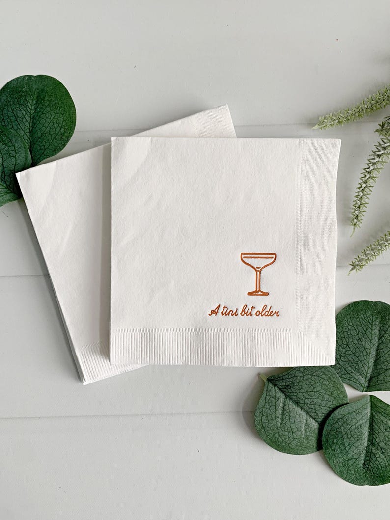 Celebrate a milestone in style with these charming A Tini Bit Older Martini Cocktail Napkins, the perfect addition to any martini-themed birthday party or sophisticated gathering. Designed for lovers of elegant cocktails, these foil-stamped napkins feature a chic illustration of a classic coup martini glass wrapped with a delicate bow around the stem, adding a playful yet refined touch to your celebration. These are perfect for any age birthday, give them as gift for the martini lover.