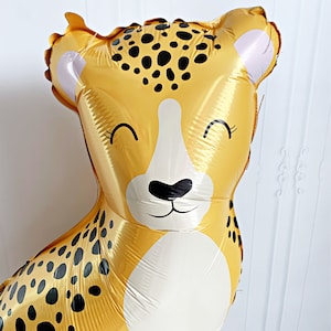 K&ouml;nnte beinhalten: Ein gro&szlig;er, goldfarbener Ballon in Form eines Geparden mit schwarzen Flecken und wei&szlig;en Akzenten. Der Ballon hat ein l&auml;chelndes Gesicht mit geschlossenen Augen. Ideal f&uuml;r eine Geburtstagsfeier oder eine festliche Veranstaltung.