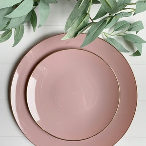 Puede incluir: Dos platos de cena de cer&aacute;mica rosa con borde dorado. Los platos est&aacute;n apilados uno encima del otro.