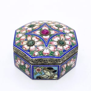 May include: An octagonal jewelry box with a floral design. The box features pink and white flowers, green and red gemstones, and a blue border. The sides of the box have a decorative pattern and a small image of a person.