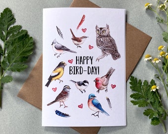May include: A white card with the text "Happy Bird-Day!" surrounded by illustrations of various birds, including an owl, a chickadee, a cardinal, and a bluebird. There are also small red hearts scattered around the birds.