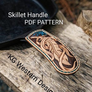 May include: A leather skillet handle with a carved feather design. The handle is tan with dark brown accents and teal stitching. The text "Skillet Handle PDF PATTERN" is visible.