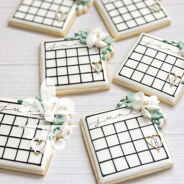 1 docena de galletas de azúcar con diseño de calendario nupcial, flores, follaje y caligrafía para anunciar la fecha de la boda.