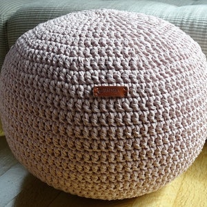 May include: A pink crocheted pouf ottoman with a brown leather tag that says "Handmade with Love".