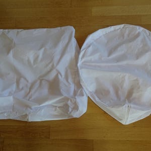 Puede incluir: Dos fundas de silla de tela blanca. Una funda es rectangular y la otra es redonda.