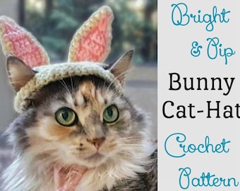 Può includere: Primo piano di un gatto che indossa un cappello da coniglio all'uncinetto con orecchie rosa. Il cappello è bianco con un motivo rosa chiaro e crema. Il testo "Bright & Dip Bunny Cat-Hat Crochet Pattern" è sullo sfondo.