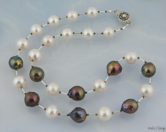 Puede incluir: Un collar de perlas de dos hilos con una mezcla de perlas blancas y oscuras iridiscentes. Las perlas están ensartadas en una delicada cadena de plata con pequeñas cuentas de metal. El collar se asegura con un cierre decorativo.