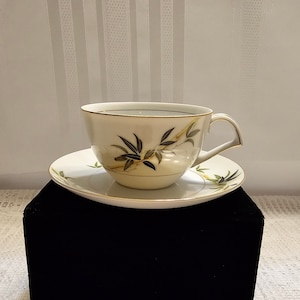May include: A white teacup and saucer with a gold rim and a green and gold bamboo design.