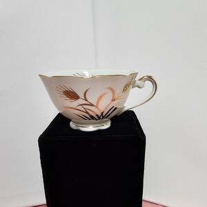 May include: A white teacup with a gold floral design. The cup has a scalloped rim and a small foot.