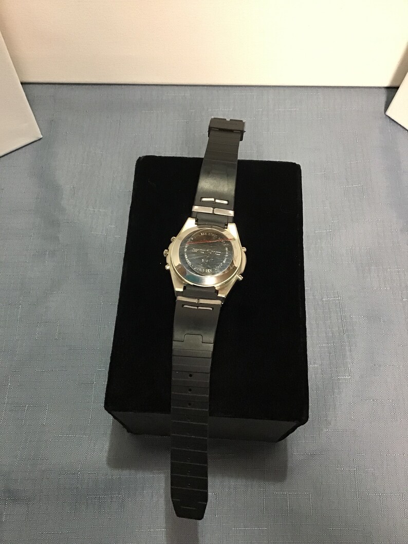 May include: A silver and black wristwatch with a black rubber strap. The watch is on a black velvet display stand.