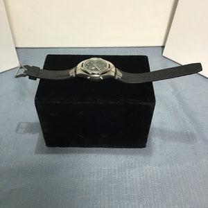 May include: A silver and black wristwatch with a black rubber strap. The watch has a digital display and multiple chronograph functions.