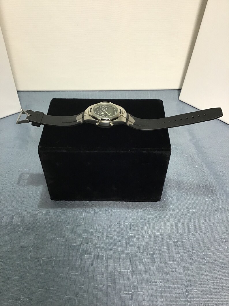 May include: A silver and black wristwatch with a black rubber strap. The watch has a digital display and multiple chronograph functions.