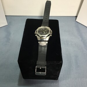May include: A silver and black wristwatch with a black rubber strap. The watch has a digital display and is sitting on a black velvet box.