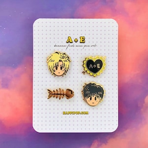 May include: A set of four gold-coloured enamel pins featuring a banana fish theme. The pins include a heart with an arrow, a fish skeleton, and two character portraits. The text "A+E banana fish mini pin set" and "happippop.com" are printed on the card.