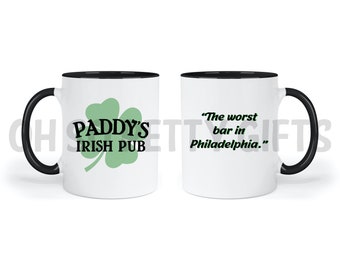 May include: White ceramic coffee mug with a black rim and handle. One side features a green shamrock with the text "Paddy's Irish Pub". The other side features the text "The worst bar in Philadelphia."