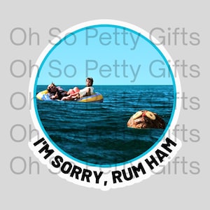 May include: A round sticker featuring a scene of two people in a yellow inflatable raft on the ocean. A large, round object resembling a ham floats nearby. The text "I'M SORRY, RUM HAM" is printed on the sticker.