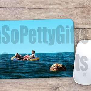 May include: A blue and yellow inflatable raft with two people on it in the ocean. A brown coconut with two eyes and a mouth is floating in the water.