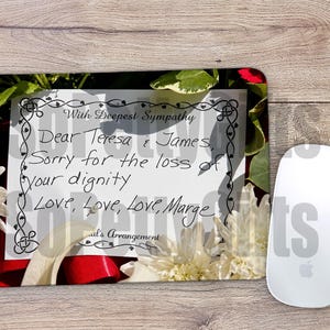 May include: A rectangular mouse pad featuring a floral background with white chrysanthemums and red ribbons. The center displays a white card with a black decorative border and the text: With Deepest Sympathy, Dear Teresa & James, Sorry for the loss of your dignity, Love, Love, Love, Marge, Paul's Arrangement.