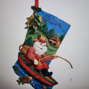 May include: A blue and green felt Christmas stocking with a Santa Claus figure fishing from a red boat. The stocking has a name, "Brian", embroidered on the front and the words "S.S. SANTA" on the bottom.