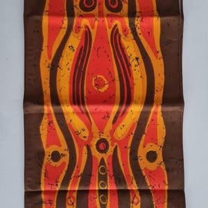 Könnte beinhalten: Ein brauner Wandbehang aus Stoff mit einem farbenfrohen abstrakten Design. Das Design zeigt eine zentrale Figur mit einem Farbschema aus Rot, Orange und Gelb. Die Figur ist von kleineren Kreisen und Linien umgeben.