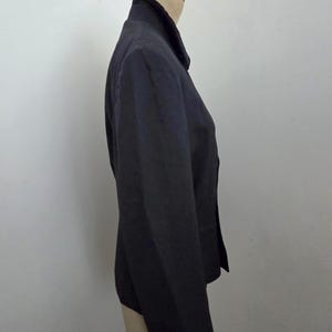 Puede incluir: Un blazer negro exhibido en un maniqu&iacute;. El blazer tiene solapas con muescas, mangas largas y cierre de dos botones. La tela parece tener una textura sutil. El blazer es de estilo cl&aacute;sico, adecuado para diversas ocasiones.