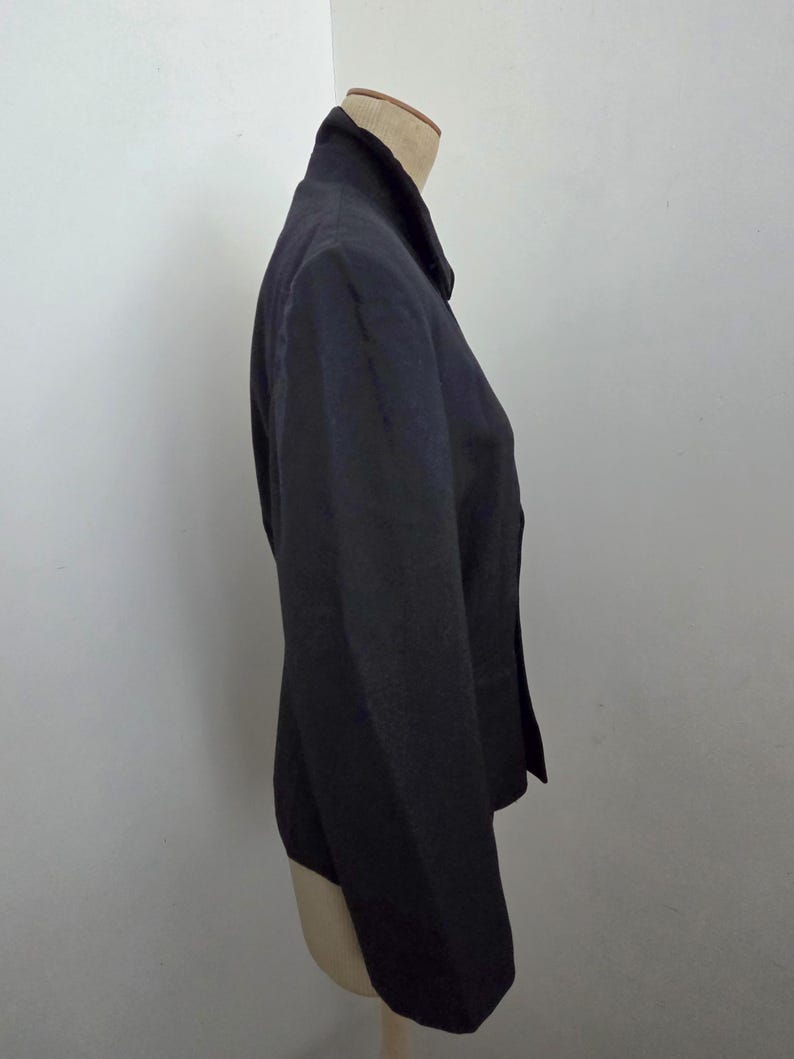 Puede incluir: Un blazer negro exhibido en un maniqu&iacute;. El blazer tiene solapas con muescas, mangas largas y cierre de dos botones. La tela parece tener una textura sutil. El blazer es de estilo cl&aacute;sico, adecuado para diversas ocasiones.