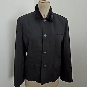 Puede incluir: Un blazer negro con cuello de terciopelo, exhibido en un maniqu&iacute;. El blazer tiene cierre de tres botones, dos bolsillos delanteros y un corte entallado. El cuello es de un color oscuro contrastante, agregando un toque de elegancia al dise&ntilde;o cl&aacute;sico.