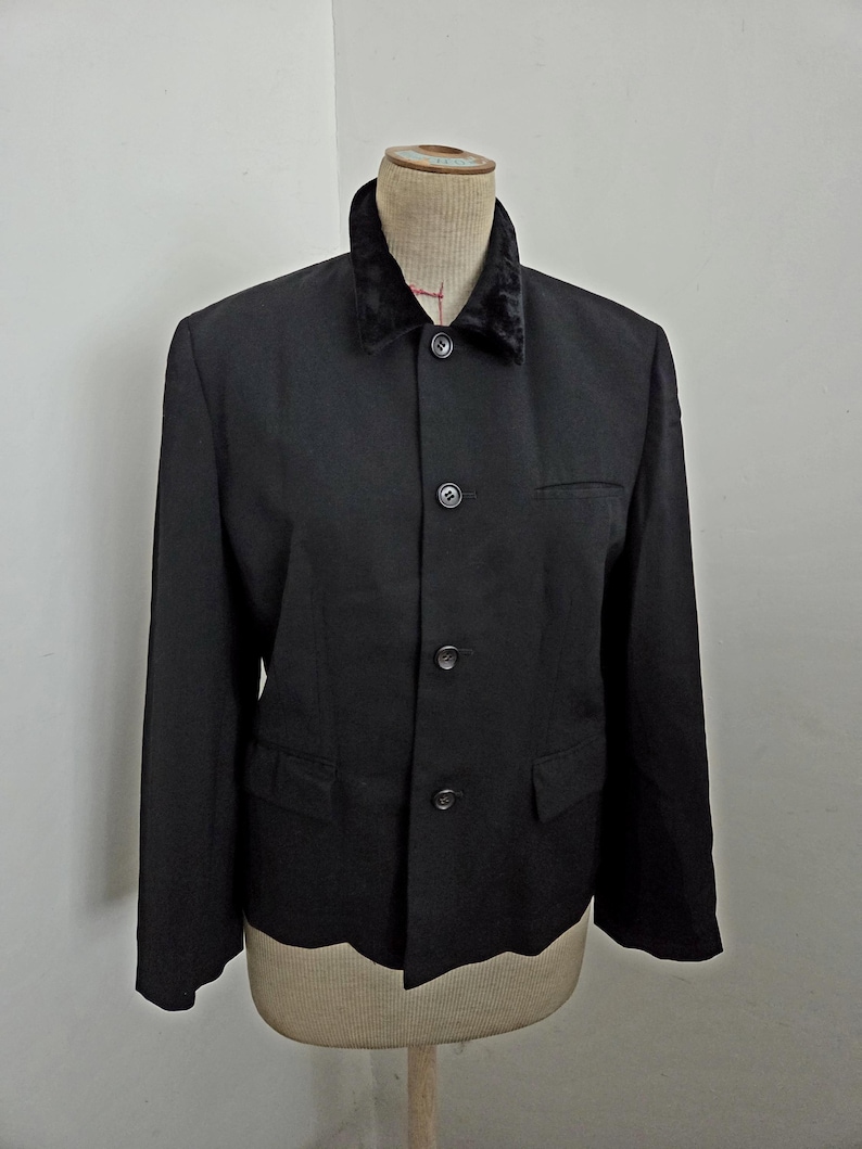 Puede incluir: Un blazer negro con cuello de terciopelo, exhibido en un maniqu&iacute;. El blazer tiene cierre de tres botones, dos bolsillos delanteros y un corte entallado. El cuello es de un color oscuro contrastante, agregando un toque de elegancia al dise&ntilde;o cl&aacute;sico.