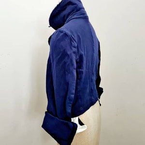 May include: A navy blue cropped jacket with a high collar and long sleeves. The jacket has a slightly distressed look and features a button closure.