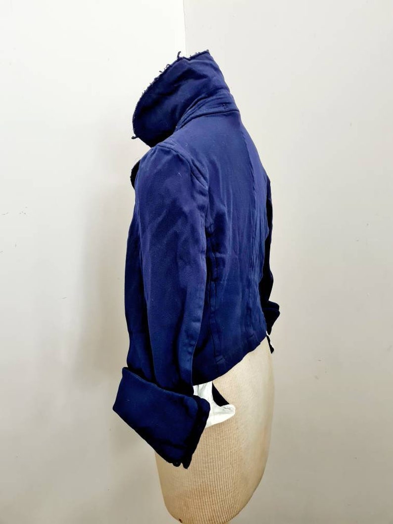 May include: A navy blue cropped jacket with a high collar and long sleeves. The jacket has a slightly distressed look and features a button closure.