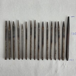 Op de afbeelding: Een set van 18 metalen gereedschappen met verschillende puntvormen, in een rij op een wit oppervlak gelegd. De gereedschappen zijn ongeveer 10 cm lang.