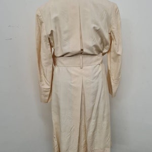 May include: A long-sleeved, cream-coloured coat with a belt and a single back vent.