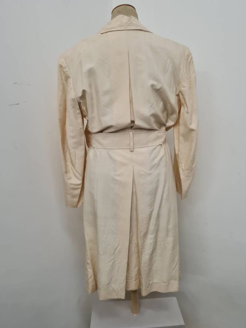 May include: A long-sleeved, cream-coloured coat with a belt and a single back vent.
