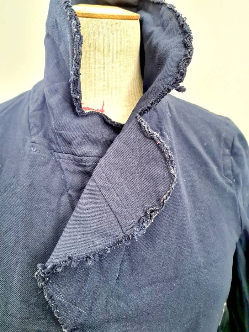 May include: A navy blue jacket with a frayed collar. The collar is folded over and the jacket is on a mannequin.