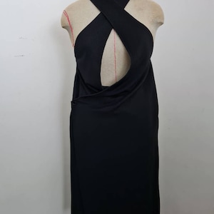 May include: A black sleeveless dress with a criss-cross halter neckline and a keyhole cutout at the back. The dress has a wrap-style skirt and a button fastening on the side.