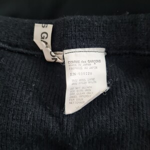 Pode incluir: Um su&eacute;ter de malha preto com uma etiqueta branca que diz "COMME des GARCONS MADE IN JAPAN FABRIQUE AU JAPON EN-030220 75% WOOL LAINE 25% NYLON NYLON DO NOT BLEACH USE COOL IRON DRY CLEAN ONLY JAVEL INTERDIT FER DOUX NETTOYAGE"