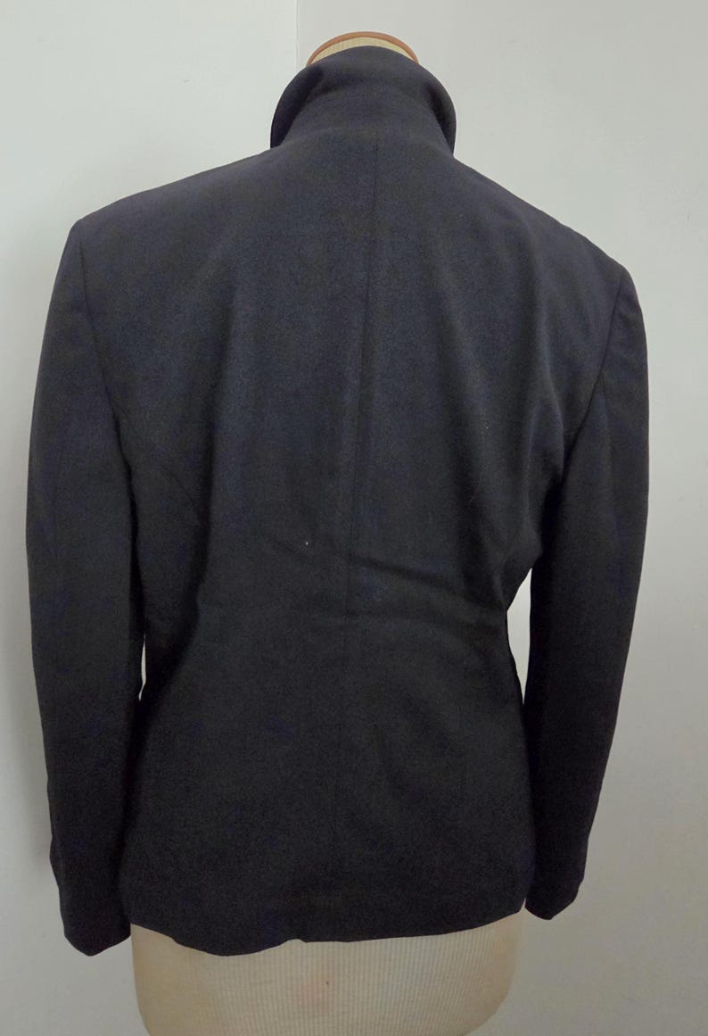 Puede incluir: Un blazer azul marino oscuro con cuello alto, visto desde atr&aacute;s. La chaqueta a medida tiene mangas largas y un dise&ntilde;o cl&aacute;sico. El blazer se exhibe en un maniqu&iacute;.