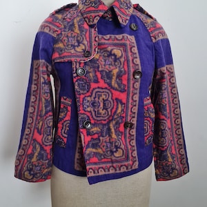 May include: A vintage jacket with a striking paisley pattern in red, gold, and purple. The jacket features a double-breasted design with dark buttons and a unique asymmetrical closure. The collar and sleeves are also patterned.