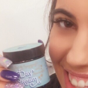 May include: A close-up of a blue and white jar with the text "Day Dream" on it. The jar is being held by a person with their hand visible in the image. The person is wearing nail polish with glitter and purple accents.
