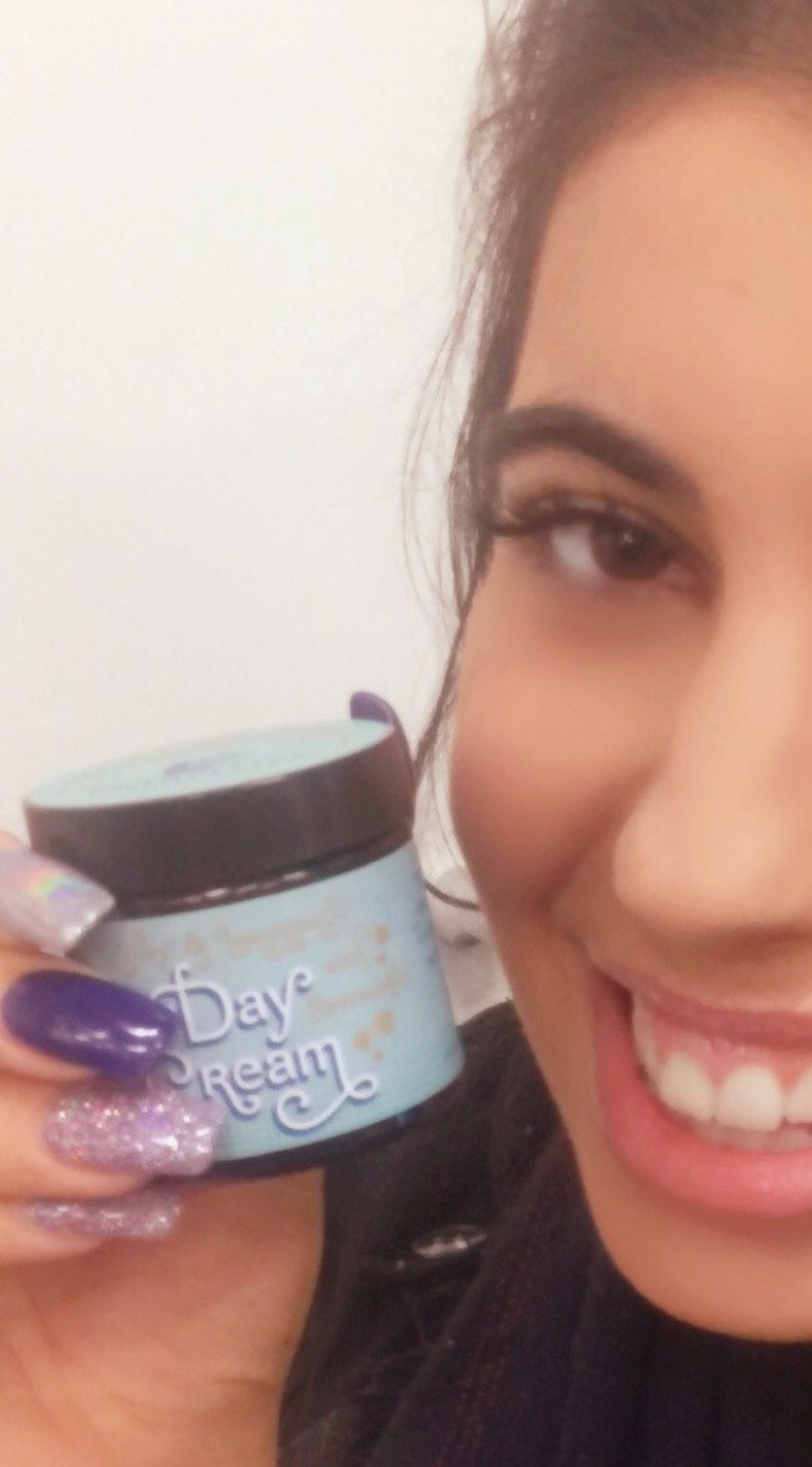 May include: A close-up of a blue and white jar with the text "Day Dream" on it. The jar is being held by a person with their hand visible in the image. The person is wearing nail polish with glitter and purple accents.