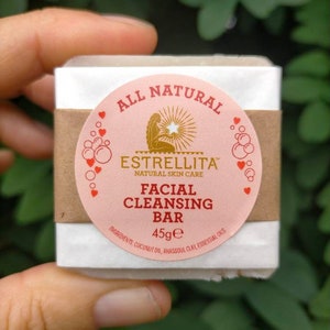 May include: A pink and brown bar soap with the words "All Natural" and "Estrellita Natural Skin Care" on the label. The soap is labeled "Facial Cleansing Bar" and is 45 grams. The ingredients are listed as coconut oil, rhassoul clay, and essential oils.